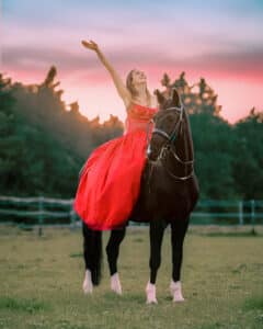 Reiterin in langem roten Kleid im Sonnenuntergang